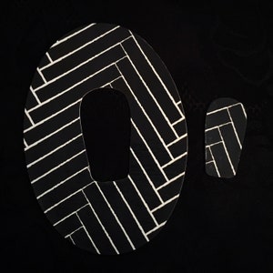 May include: Black and white geometric pattern on a pair of fabric patches. The larger patch is shaped like a rounded rectangle with a hole in the center. The smaller patch is a rectangle.