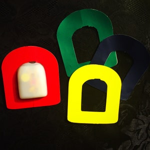 Può includere: Quattro forme colorate ritagliate, che ricordano i copri-chiavi, in verde, giallo, blu e rosso. Le forme sono disposte a semicerchio, con la forma rossa in basso e la forma verde in alto.