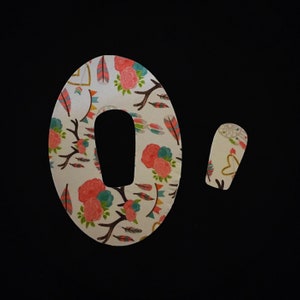 May include: Two patterned medical patches with a floral and feather design. The larger patch has an oval shape with a cutout, while the smaller one is rectangular. The patches feature pink, teal, and brown accents on a white background.