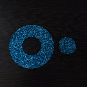 May include: Two blue glitter circles, one larger than the other, with a hole in the center of the larger circle.