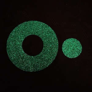 May include: Two green glitter circles, one with a hole in the center, on a black background.