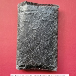 May include: A black leather wallet with a worn and textured surface. The wallet shows signs of everyday use after three years.