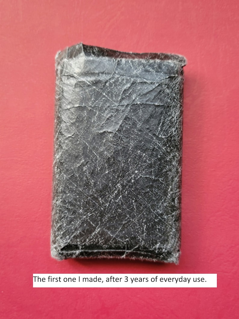 May include: A black leather wallet with a worn and textured surface. The wallet shows signs of everyday use after three years.
