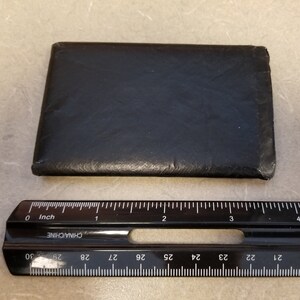 May include: A black leather wallet with a smooth surface. The wallet is approximately 3.5 inches wide and 2.5 inches tall.