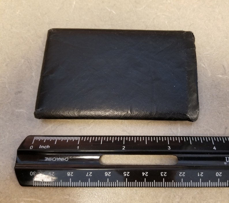 May include: A black leather wallet with a smooth surface. The wallet is approximately 3.5 inches wide and 2.5 inches tall.