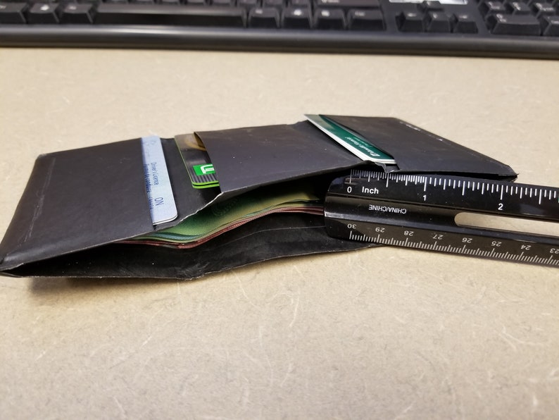 May include: A black leather wallet with multiple cards and cash inside. The wallet is open and a ruler is placed next to it. The ruler is marked in inches and centimeters.