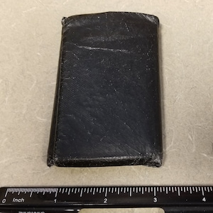May include: A black leather wallet with a worn and distressed look. The wallet is closed and appears to be made of a high-quality material.