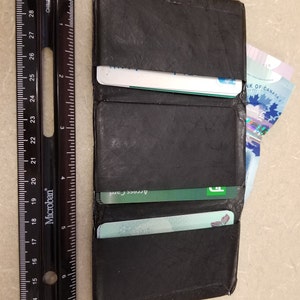 May include: A black leather wallet with a flap closure. The wallet is open and contains several cards, including a green Access Card and a blue Ontario card. A Canadian banknote is visible in the right side of the wallet.