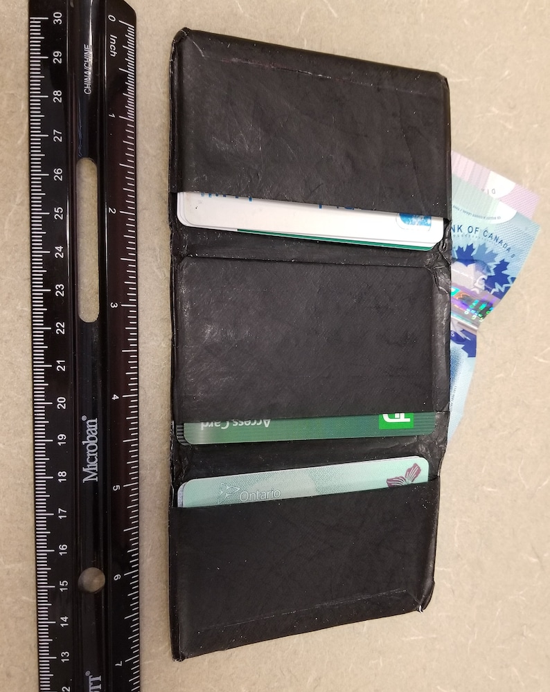 May include: A black leather wallet with a flap closure. The wallet is open and contains several cards, including a green Access Card and a blue Ontario card. A Canadian banknote is visible in the right side of the wallet.
