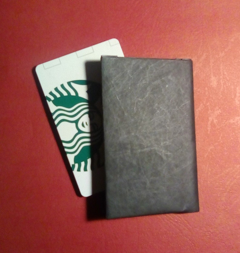 May include: A white card with the Starbucks logo in green. The card is partially covered by a black leather notebook.