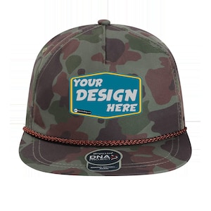 Op de afbeelding: Een camouflagegroene en bruine baseballpet met een bruine touwrand. De pet heeft een vierkant patch met de tekst "YOUR DESIGN HERE" in wit en blauw op een gele achtergrond. De pet heeft ook een klein logo met de tekst "DNA PROJECT" in wit op een rode achtergrond.