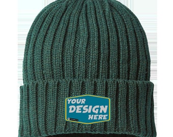 Könnte beinhalten: Dunkelgrüne, gerippte Strickmütze mit einem rechteckigen Aufnäher. Der Aufnäher hat einen gelben Rand und die Worte "YOUR DESIGN HERE" in Weiß und Blaugrün. Die Mütze ist aus einem weichen, strukturierten Material gefertigt.