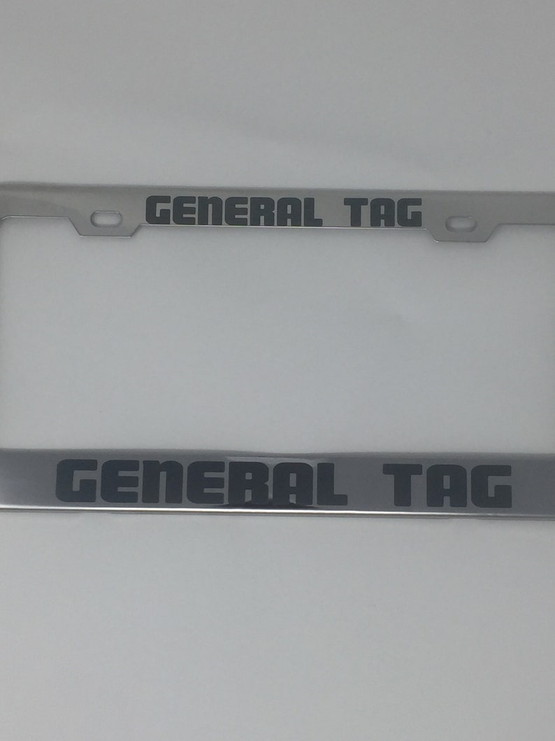 May include: A silver license plate frame with the text "GENERAL TAG" in black lettering on the top and bottom of the frame.