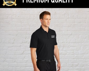 May include: A black polo shirt with a white embroidered logo that says "LOGO HERE". The shirt is worn by a person standing in front of a white brick wall.