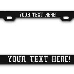 May include: Black metal license plate frame with white text that reads "YOUR TEXT HERE!" on the top and bottom.