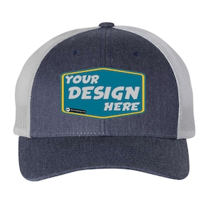 May include: A navy blue and white trucker hat with a yellow and teal patch that says "YOUR DESIGN HERE".