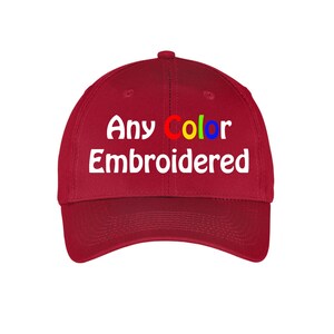 May include: Red baseball cap with white embroidery that reads "Any Color Embroidered". The word "Color" is embroidered in rainbow colors.