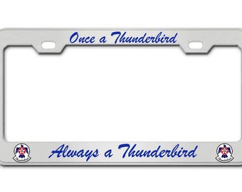 Könnte beinhalten: Silberner Kennzeichenrahmen mit dem Text "Once a Thunderbird" oben und "Always a Thunderbird" unten in blauer Schrift. Enthält Thunderbird-Logos auf jeder Seite.