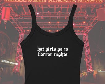 May include: Black tank top with the text "hot girls go to horror nights" in white gothic font. The top has thin straps and a scoop neckline. The background features a red lit sign that says "Halloween Horror Nights".