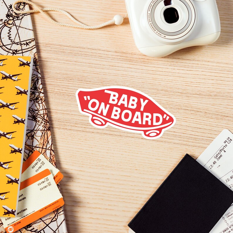 Peut inclure: Autocollant rouge et blanc avec le texte "Baby On Board" en police blanche sans empattement. L'autocollant a la forme d'une planche &agrave; roulettes.