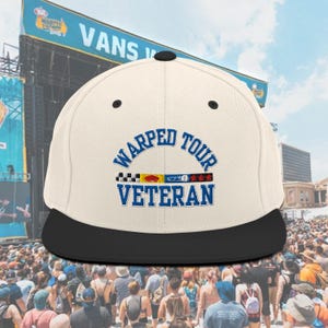May include: A white and black baseball cap with the text "WARPED TOUR VETERAN" in blue embroidery. The cap has a black brim and a white crown with a band of colorful patches.