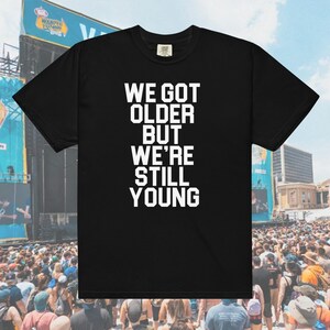 May include: Black t-shirt with white text that reads "We got older but we're still young".