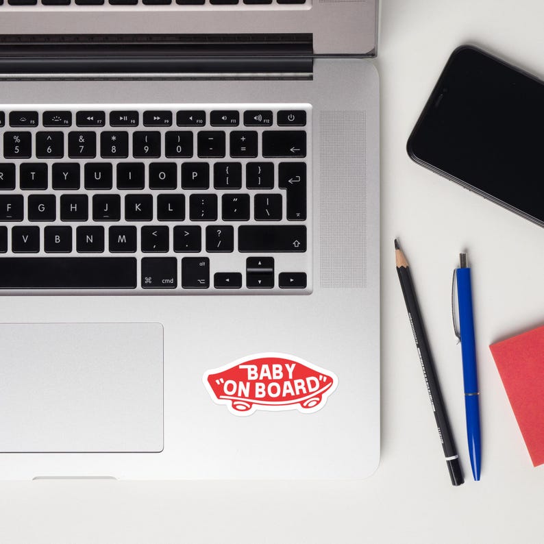 Op de afbeelding: Een witte laptop met een zwart toetsenbord en een rode sticker met de tekst "Baby on Board" in de rechterbenedenhoek van de laptop.