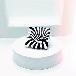 Peut inclure: Un objet sculptural abstrait &agrave; rayures noires et blanches ressemblant &agrave; une fleur ou &agrave; une chaise. L'objet est pos&eacute; sur un pi&eacute;destal blanc.