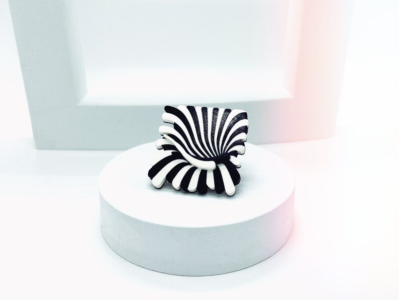 Peut inclure: Un objet sculptural abstrait &agrave; rayures noires et blanches ressemblant &agrave; une fleur ou &agrave; une chaise. L'objet est pos&eacute; sur un pi&eacute;destal blanc.