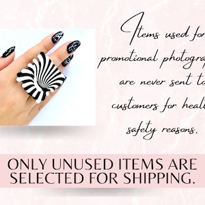 Peut inclure: Une bague noire et blanche avec un motif en spirale. La bague est port&eacute;e sur une main avec un vernis &agrave; ongles noir. Le texte "Items used for promotional photography are never sent to customers for health safety reasons. ONLY UNUSED ITEMS ARE SELECTED FOR SHIPPING." est affich&eacute; sous l'image.