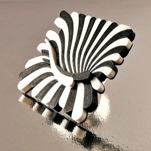 Peut inclure: Une sculpture abstraite en 3D imprim&eacute;e en noir et blanc ressemblant &agrave; une chaise stylis&eacute;e. La sculpture a un design en forme d'&eacute;ventail avec des lignes courbes et un centre creux.