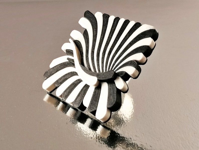 Peut inclure: Une sculpture abstraite en 3D imprim&eacute;e en noir et blanc ressemblant &agrave; une chaise stylis&eacute;e. La sculpture a un design en forme d'&eacute;ventail avec des lignes courbes et un centre creux.