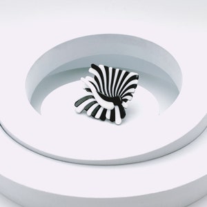 Peut inclure: Une sculpture abstraite noire et blanche avec un design en spirale. La sculpture est pos&eacute;e sur une plateforme blanche avec une ouverture circulaire.