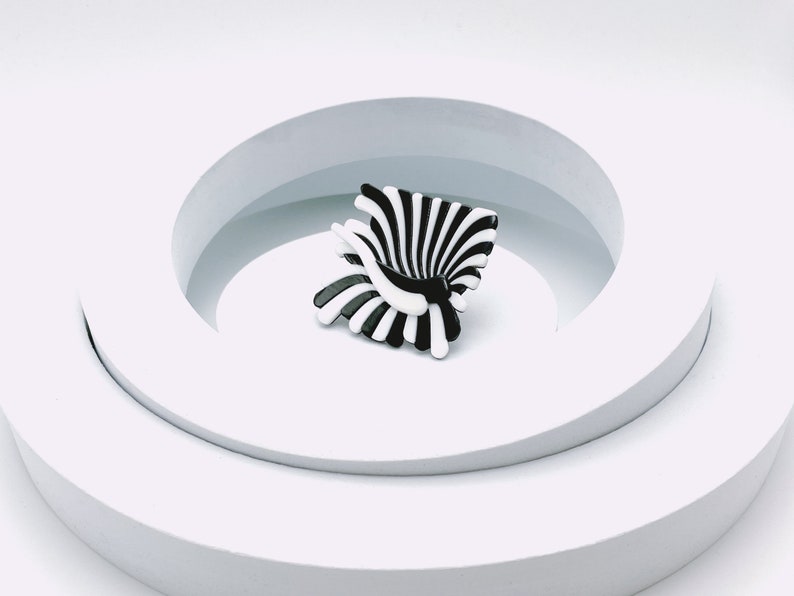 Peut inclure: Une sculpture abstraite noire et blanche avec un design en spirale. La sculpture est pos&eacute;e sur une plateforme blanche avec une ouverture circulaire.