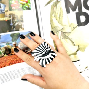Peut inclure: Une bague noire et blanche avec un motif g&eacute;om&eacute;trique. La bague est en plastique et a une finition brillante.