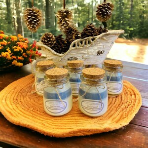 May include: Six small glass jars with cork lids filled with layered blue and white candles. The jars are arranged on a round, woven, orange mat. The candles are labeled "Cedarwood".