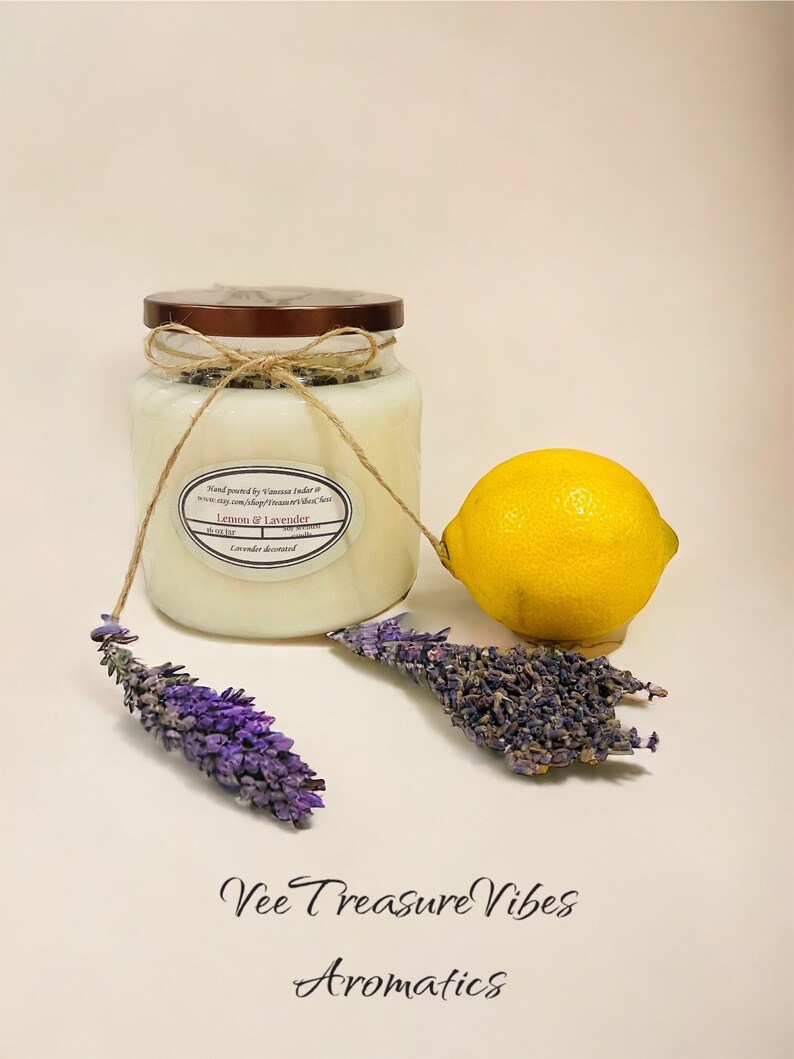 May include: A glass jar candle with a brown lid and a white label that reads "Hand poured by Vanessa Indar", "Lemon & Lavender", and "Lavender decorated". The candle is next to a lemon and dried lavender sprigs.