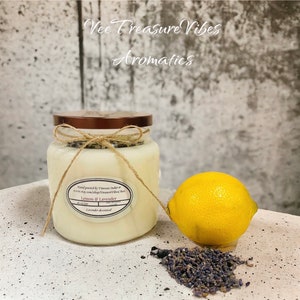 May include: A clear glass jar candle with a brown lid and a twine bow. The candle is labeled "Lemon & Lavender" and is decorated with lavender. A yellow lemon and dried lavender flowers are in the foreground.