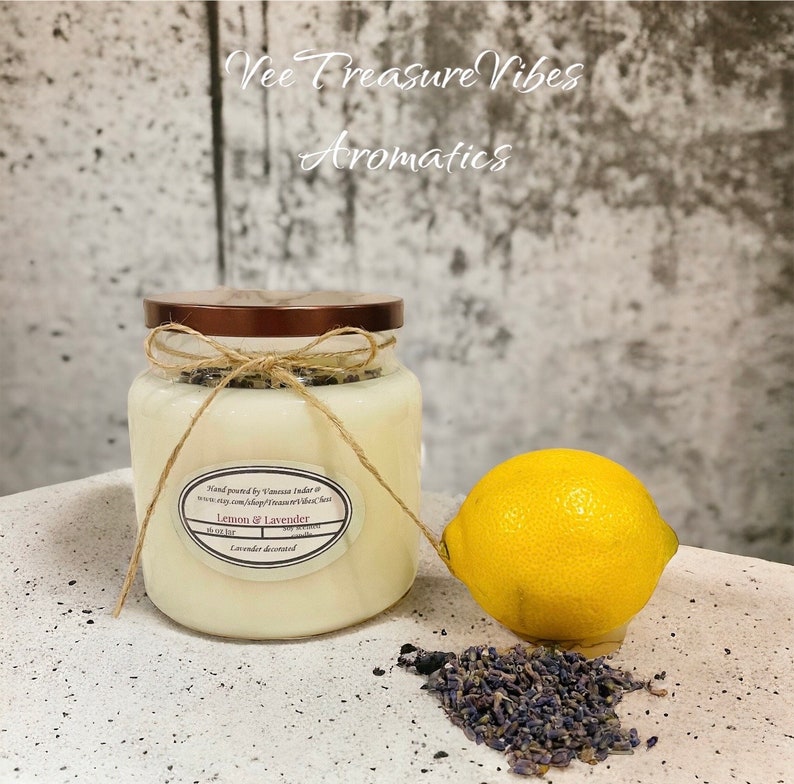 May include: A clear glass jar candle with a brown lid and a twine bow. The candle is labeled "Lemon & Lavender" and is decorated with lavender. A yellow lemon and dried lavender flowers are in the foreground.