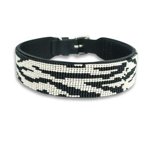 May include: Black leather dog collar with a white and black beaded pattern. The collar has a silver buckle.
