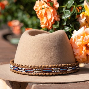 May include: A tan felt fedora hat with a brown leather band and a blue, white, and red beaded trim.
