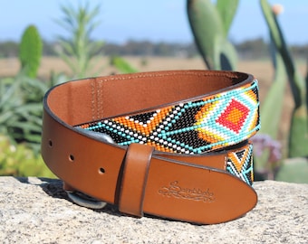May include: A brown leather belt with a colorful beaded design featuring geometric patterns in shades of turquoise, orange, red, white, and black. The belt buckle is silver and the leather is embossed with the word "Sambboho".