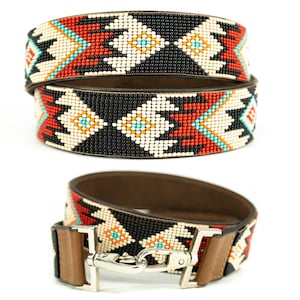 May include: A brown leather strap with a colorful beaded design. The strap features a geometric pattern in shades of black, white, red, orange, and turquoise. The strap has a metal clasp.