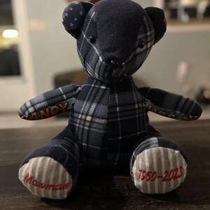 Peut inclure: Un ours en peluche fait &agrave; la main, orn&eacute; d'un motif &agrave; carreaux bleu marine. Le visage de l'ours est noir, avec le mot "ANDY" brod&eacute; sur un bras et les dates "1950-2023" et "Mawmaw" brod&eacute;es sur les pieds. Les oreilles ont un motif d'&eacute;toiles.