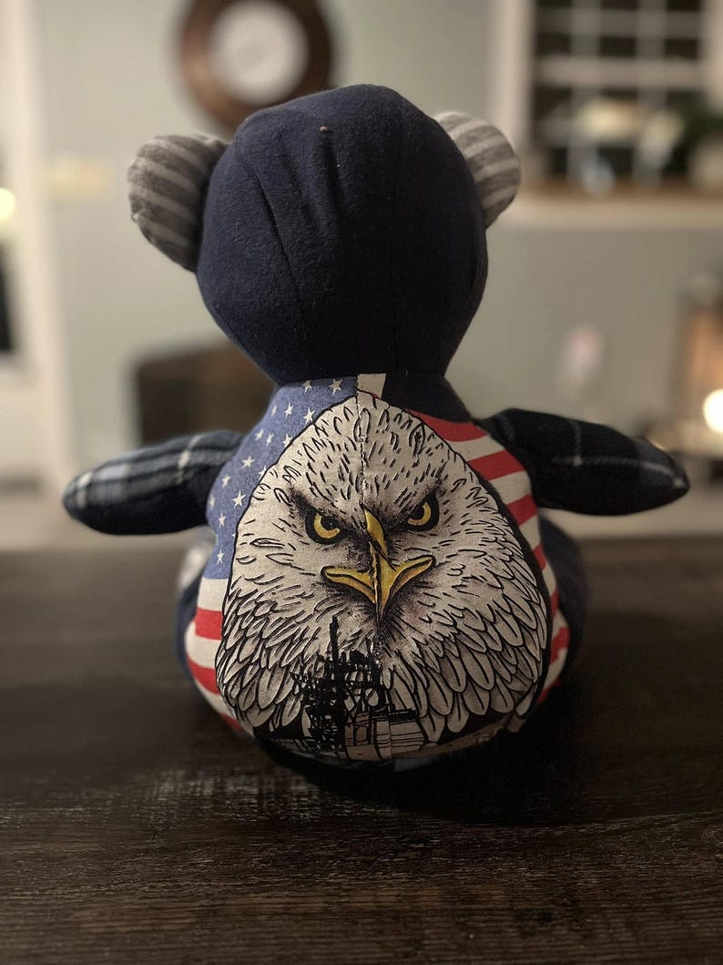 Peut inclure: Un ours en peluche patriotique avec une t&ecirc;te bleu marine et des oreilles ray&eacute;es. La poitrine de l'ours pr&eacute;sente un graphique d&eacute;taill&eacute; d'un aigle avec le drapeau am&eacute;ricain. Les bras de l'ours sont &agrave; carreaux.