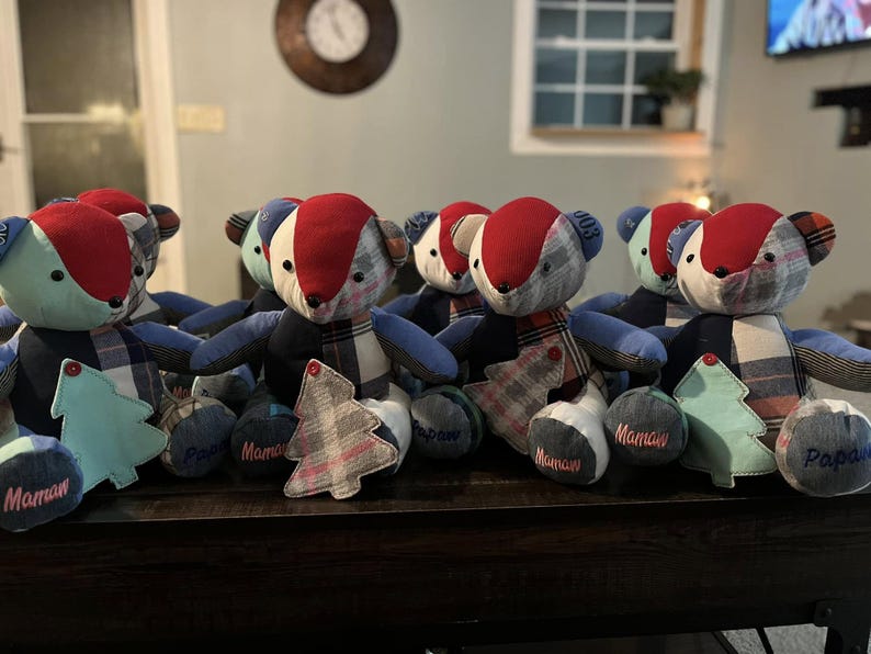 Peut inclure: Plusieurs ours en peluche faits &agrave; la main avec des d&eacute;tails en tissu rouge, bleu et &agrave; carreaux. Chaque ours a un design unique et est accompagn&eacute; d'un petit arbre d&eacute;coratif et d'un coussin rond avec le mot "Maman" ou "Papa" brod&eacute;.