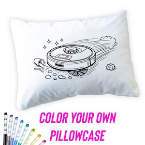 May include: White pillowcase with a black and white illustration of a robot vacuum cleaner in action. The pillowcase has the text "COLOR YOUR OWN PILLOWCASE" in pink. A set of colorful markers are in the foreground.