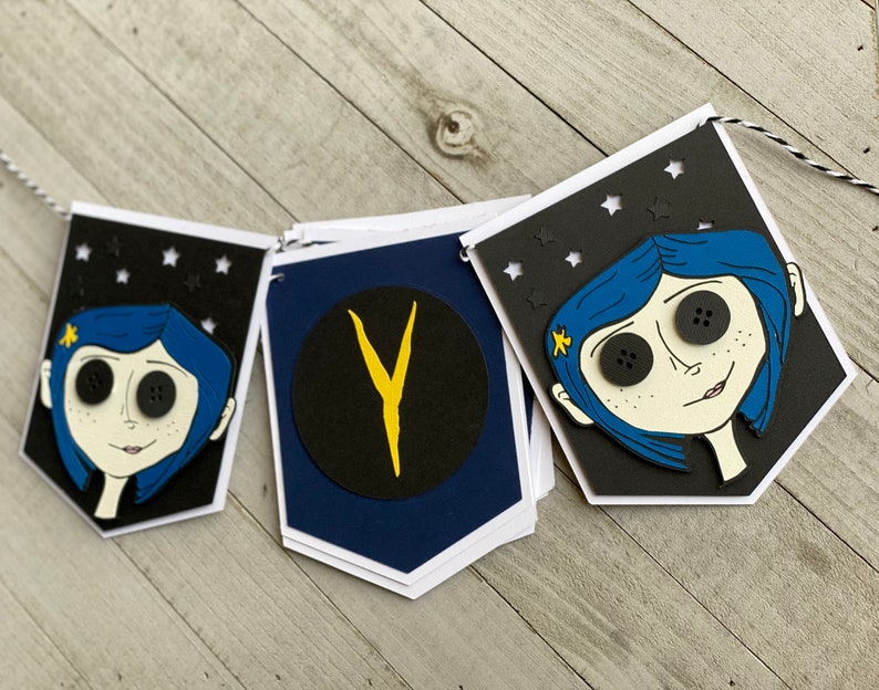 May include: A black and white banner with a blue-haired girl with large black buttons for eyes. The banner has a black circle with a yellow "Y" in the center. The banner is decorated with white stars.