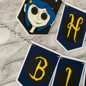 May include: A blue and black birthday banner with a character from the movie "Coraline" and the letters "Happy Birthday" in yellow on a black background.