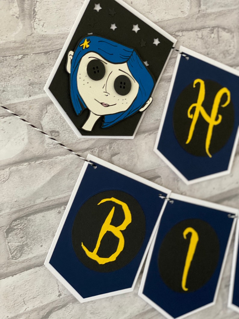 May include: A blue and black birthday banner with a character from the movie "Coraline" and the letters "Happy Birthday" in yellow on a black background.